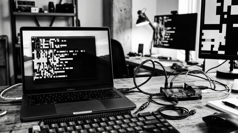 Monochrome developer desk with laptop, Raspberry Pi, and connected AI tooling